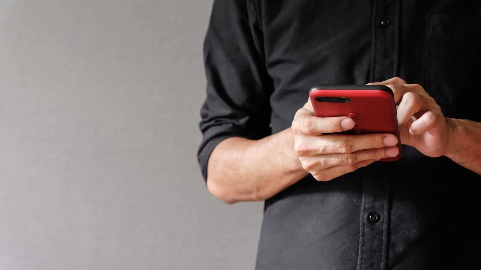 Homem de camisa preta digitando num celular vermelho.